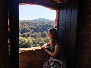 Young woman looking through window against landscape