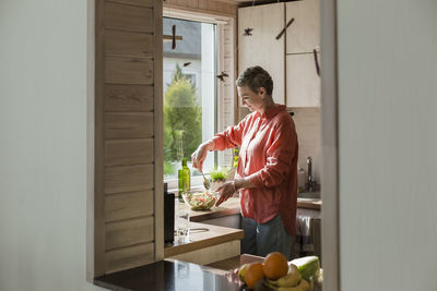 Woman at the window in kitchen preparing salad