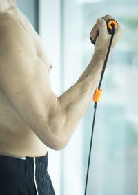 Midsection of shirtless man stretching resistance band in gym