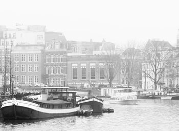 Boats moored in river by buildings in city against clear sky