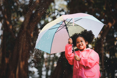 Smiling girl holding umbrella while standing outdoors during rainy season