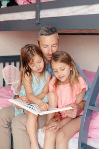 Fathers day. dad reading book to daughters girls. family of three people sitting together reading bo