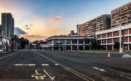 Road by buildings against sky during sunset in city