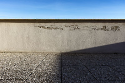 Shadow of wall on footpath against blue sky