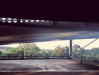 Empty road by trees against sky seen through window