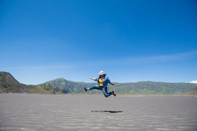 Full length of happy mid adult woman jumping on field against blue sky during sunny day