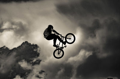 Man performing bicycle stunt against sky
