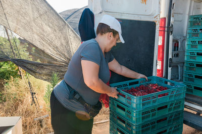 Side view of female farmer loading plastic crates in trunk of van while working in agricultural farm