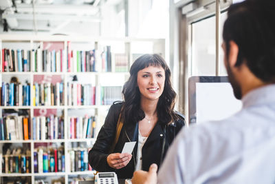 Businesswoman smiling while receiving card from male entrepreneur in office