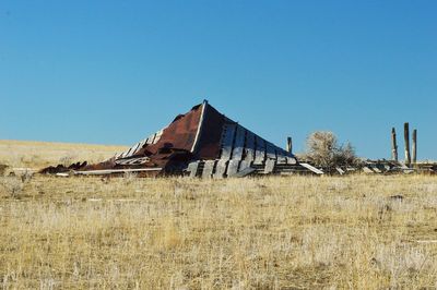 Abandoned built structure on field against clear blue sky