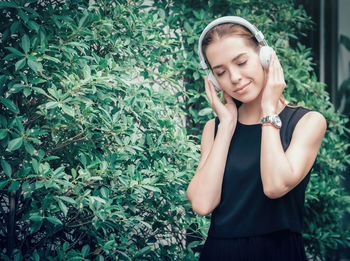 Young woman listening music while standing against plants