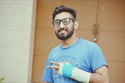 Portrait of young man gesturing peace sign with fractured hand against closed doors