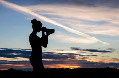 Silhouette woman photographing against sky during sunset