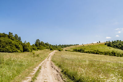 Empty road amidst field against sky