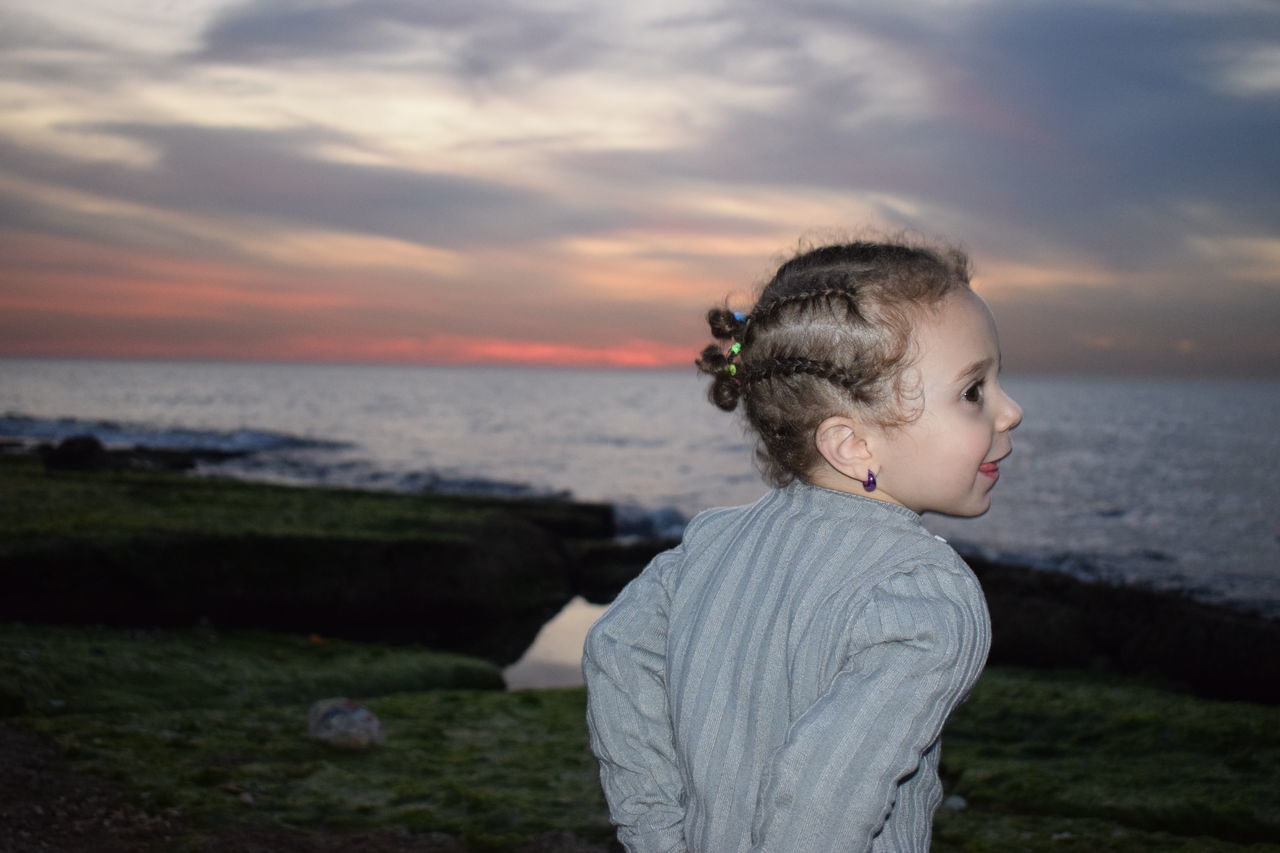 water, sea, sky, childhood, child, leisure activity, one person, lifestyles, land, real people, cloud - sky, standing, sunset, nature, beauty in nature, beach, boys, casual clothing, horizon over water, innocence, outdoors, contemplation