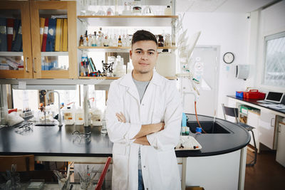 Portrait of confident young male college student standing with arms crossed in chemistry laboratory