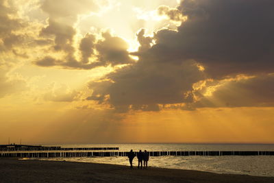 Silhouette people on beach against sky during sunset