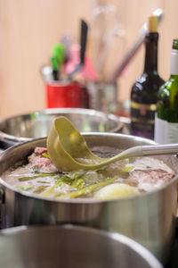 A metal saucepan filled with boiling vegetable and meat broth. there is a scoop in the broth.