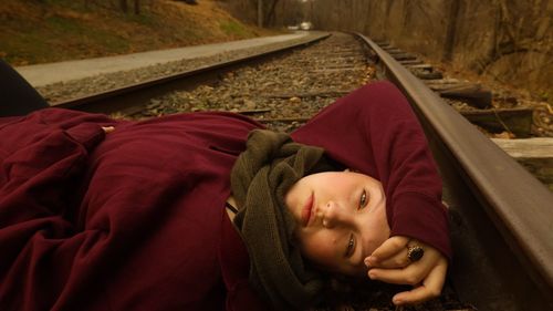 Portrait of young woman with a seductive yet solemn expression laying on railroad tracks 