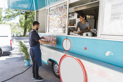 Full length of young male owner sticking poster on food truck in city