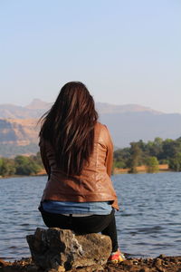 Rear view of woman sitting by lake against sky