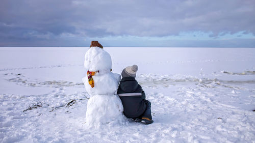 Boy sits alone with snowman and looks forward. loneliness and friend made of snow. winter mood