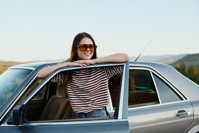 Young woman sitting on car against clear sky