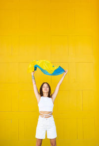 Rear view of woman with umbrella against yellow wall