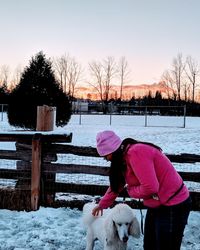 Woman with dog standing by fence during winter