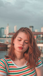 Thoughtful young woman looking down in city against sky