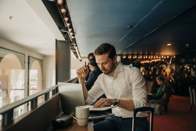 Businessman reading diary while sitting with laptop in hotel