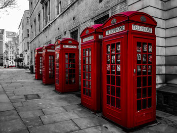 Red telephone booth on sidewalk by building in city