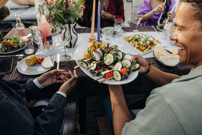 High angle view of happy man passing food plate to friend during dinner party