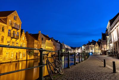 Illuminated street amidst buildings against sky at night