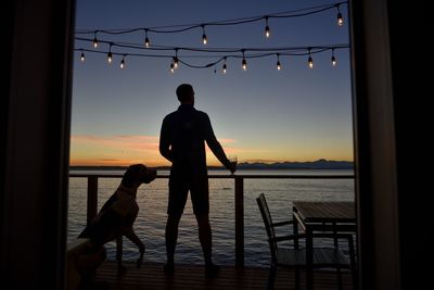 Man and dog on deck looking at lake at dusk with bulb lights overhead