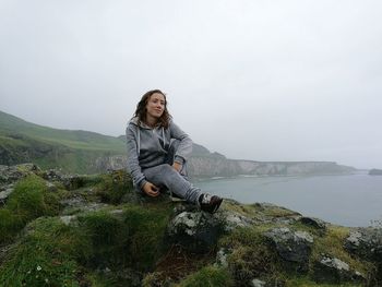 Young woman sitting on mountain at giant causeway against sky