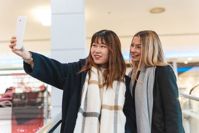 Multi-ethnic beautiful couple of girlfriends in a department store on the escalators take a selfie