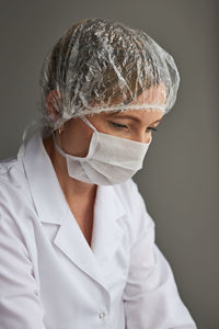 Close-up of thoughtful female doctor wearing mask looking away against gray background