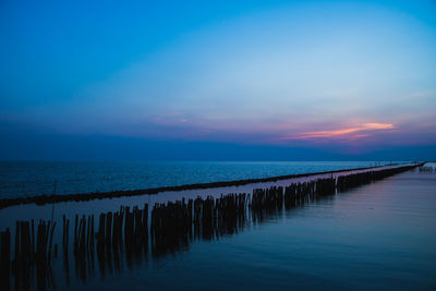 Wooden posts in sea against sky during sunset