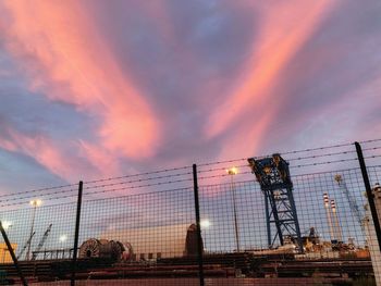 Electricity pylons against sky at sunset