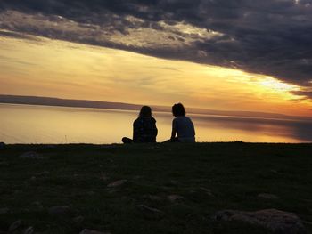 Rear view of women sitting at beach against sky during sunset