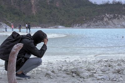 Side view of man photographing while crouching at beach