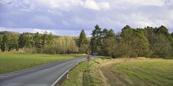 Road amidst trees on field against sky