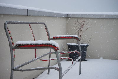 Snow covered bench against wall in back yard