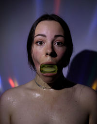 Portrait of young woman holding kiwi mouth against wall