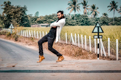 Full length portrait of young man dancing on road against trees