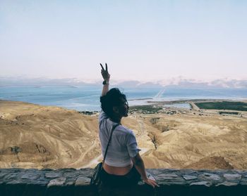 Rear view of a woman sitting on rock fence by desert against sky in israel