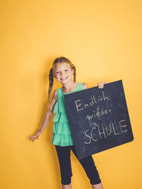 Portrait of smiling girl standing against yellow wall