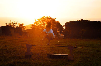 Girl jumping on bar at park against sky during sunset