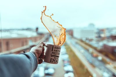 Cropped hand holding coffee cup against sky